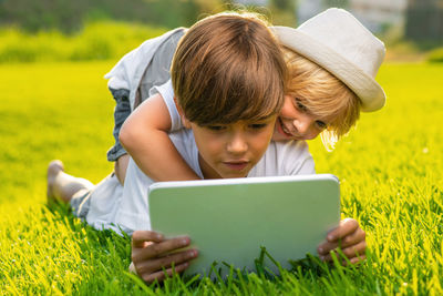 Cute sibling looking at digital tablet while lying on grass at park