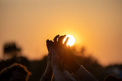 Close-up of hand holding sparkler against orange sky