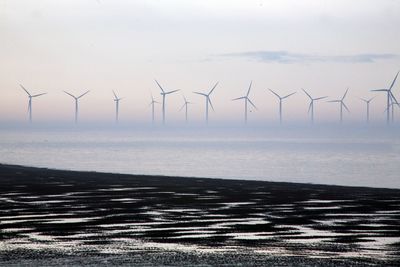 Wind turbines by sea against sky