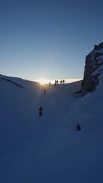 People on snowcapped mountain against clear sky during sunset