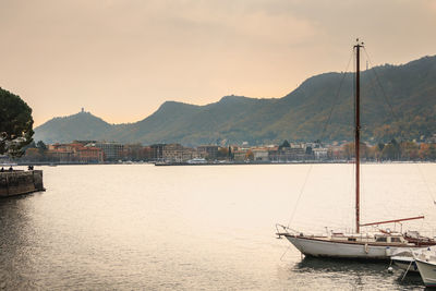 Sailboats moored on sea by mountains against sky