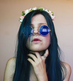 Portrait of woman wearing sunglasses while wearing flowers against wall