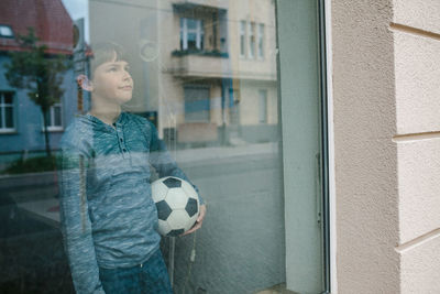 Boy playing with ball in front of window