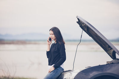 Woman talking on mobile phone while leaning over breakdown car