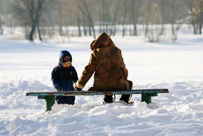 Father with son on snow covered field during sunny day