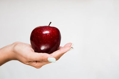 Close-up of hand holding apple against white background