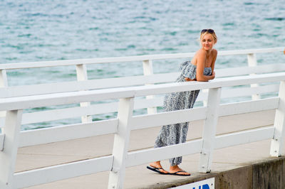 Full length on young woman leaning on railing at pier