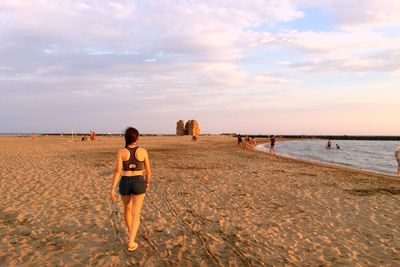 Rear view of women walking at beach against sky during sunset