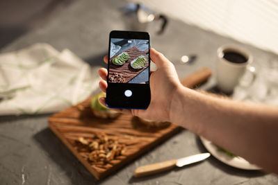 Midsection of person photographing with mobile phone on table