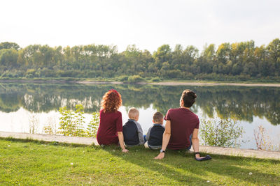Rear view of people sitting on grass by lake