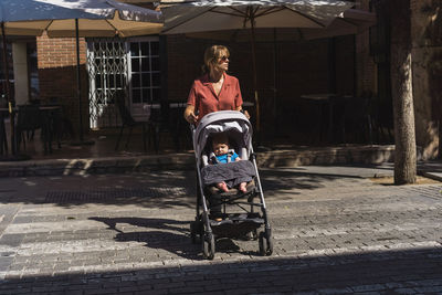 Portrait of young mother taking a walk with young baby crossing the street