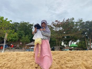 Rear view of mother and daughter on sand against trees