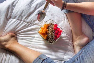 Low section of woman having fruit salad while sitting on bed at home