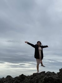 Full length of woman standing on rock against sky