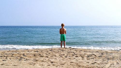 Rear view of boy standing on shore at beach