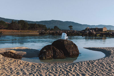 Rear view of woman sitting on beach against sky