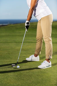 Low section of woman hitting ball with golf club on grassy field