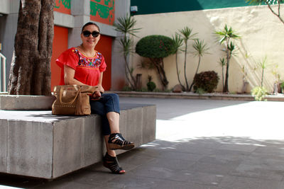 Full length portrait of smiling young woman sitting outdoors