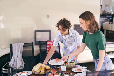 Siblings enjoying food outside motor home while camping during summer vacation