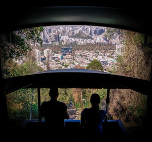 Rear view of silhouette man sitting by window in city