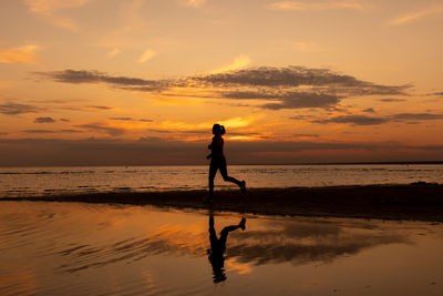 Silhouette woman walking at beach against sky during sunset