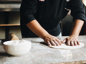 Midsection of man preparing pizza at table in home