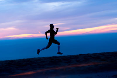 Silhouette man jumping in sea against sky during sunset