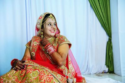 Close-up of bride sitting on chair against curtains