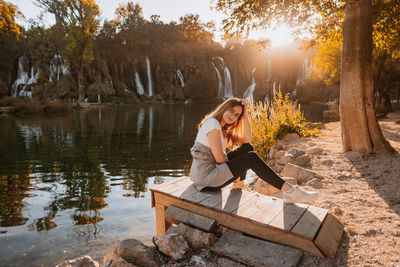 Woman sitting by lake against trees