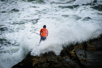 Rock fisherman braving crushing waves at auckland, new zealand muriwai beach