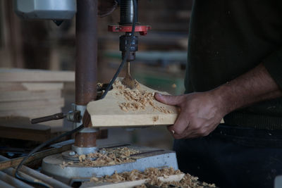 Midsection of carpenter using machinery for cutting plank at workshop