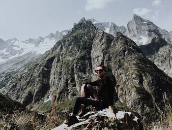 Man sitting on rock by mountains against sky