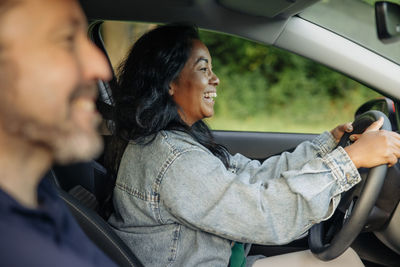 Side view of happy woman wearing denim jacket and driving car