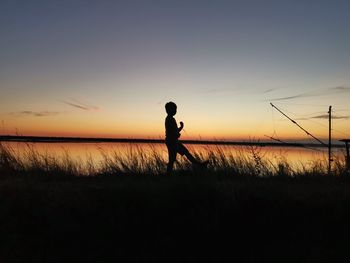 Silhouette man standing on field against sky during sunset