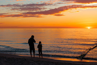 Rear view of father with daughter standing at beach during sunset