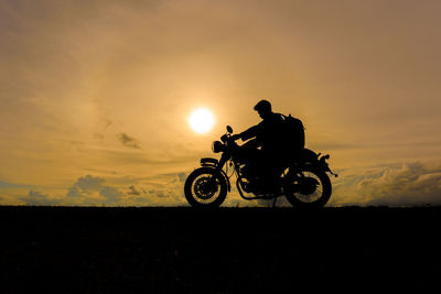 Silhouette man riding motorcycle on landscape against sky during sunset