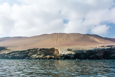 Scenic view of river by sand dunes against cloudy sky