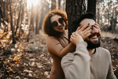 Cheerful woman closing man eyes in forest