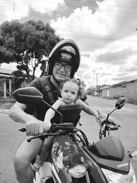 Portrait of smiling father with daughter riding motorcycle against sky