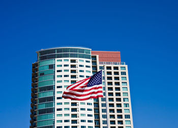 Low angle view of flag against buildings against blue sky