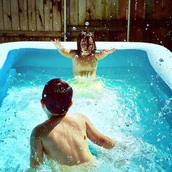 High angle view of siblings enjoying in inflatable swimming pool during sunny day