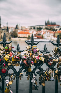 Close-up of padlocks on bridge over river against cloudy sky in city