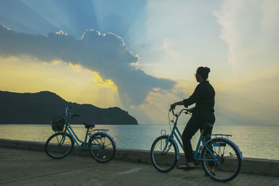 Full length of woman standing with bicycle against sea