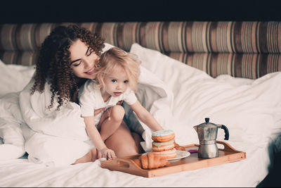 Smiling young woman embracing daughter by breakfast of bed