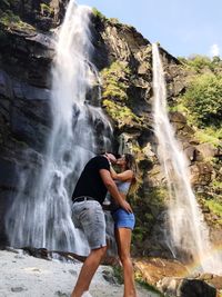 Side view of couple kissing while standing against waterfall