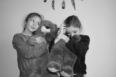 Sisters embracing teddy bears against wall at home