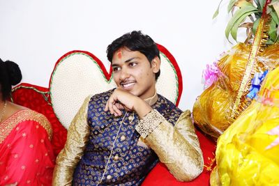 Smiling groom looking away while sitting by woman on sofa