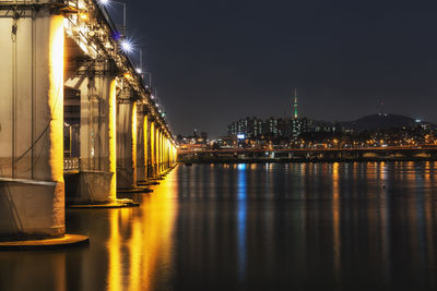 Illuminated bridge over river against sky at night