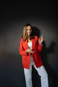 Young women in the red suit near a dark gray background points to the side with her hand