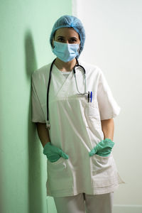 Female doctor with hands in pockets leaning by wall at clinic